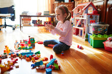 Adorable Preschooler Girl Sitting On The Floor And Playing With Colorful Construction Blocks