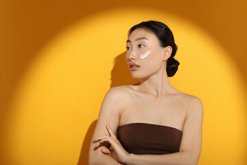 Poster - Beautiful young woman in sunlight with sun protection cream on her face against orange background, space for text