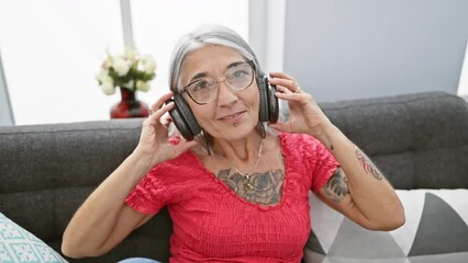 Poster - Confident middle age female joyfully taking off headphones, relaxing after enjoying music on her sofa at home