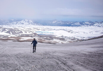 There is a man on the foreground. He is walking up. There is a chain of montains on the background.