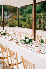 Wall Mural - Long covered festive table in the garden with bouquets of flowers and candles