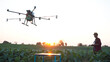 Asian farmer spraying his crops using a drone at sunset , High technology innovations for increasing productivity in agriculture.