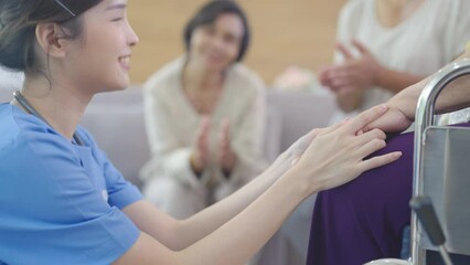 Wall Mural - Side view of nurse or doctor hold hands of senior or elderly woman who sit on wheelchair and other senior woman also clap hands in background in clinic or hospital center.