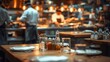 © ParinApril - A restaurant table with glasses and condiments in the foreground chefs cooking in the background.