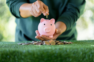 Woman hand putting coin in pink piggy bank on green bokeh background. currency, success business, investment, retirement, finance, growth loan and cash money saving for the future concepts.