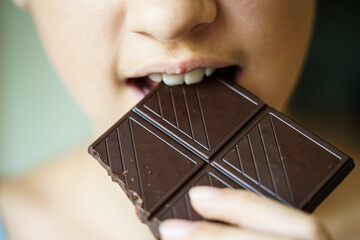 Unrecognizable young girl biting delicious chocolate bar