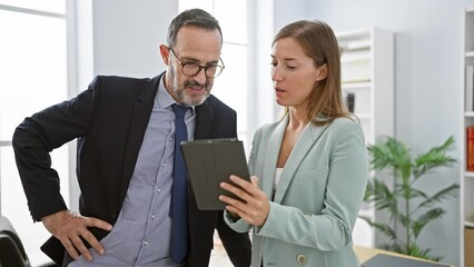 Poster - Two professional business workers, standing together indoors in the office, elegantly speaking work matters over their touchpad device. a glimpse into their successful working lifestyle.