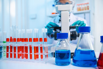 Sticker - Asian people scientist in lab coat and protective gloves working with test tubes with green and red liquids, with microscope and other test tubes in the background in laboratory.