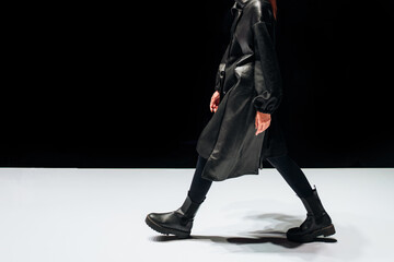 Female figure dressed in a black leather outfit walking on black background.