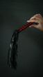 A woman's hand holds a bdsm whip on a dark background