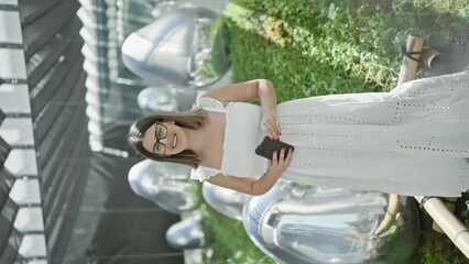 Wall Mural - Beautiful hispanic woman with glasses, immersing in futuristic tech-art exhibition at a modern museum, capturing abstract objects on smartphone