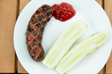 Wall Mural - Barbequed Sausage served on a plate in a garden with ketchup and fresh cucumber