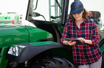Poster - Woman farmer with a digital tablet on the background of an agricultural tractor