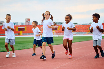 Wall Mural - Multiracial group of kids running while having exercise class at stadium.