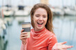 Young redhead woman holding a take away coffee at outdoors with shocked facial expression