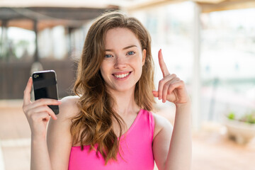 Poster - Young redhead woman using mobile phone at outdoors pointing up a great idea