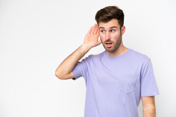 Wall Mural - Young caucasian man isolated on white background listening to something by putting hand on the ear