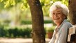 © Nemanja - Happy old aged senior woman or grandma with gray hair, sitting on the wooden bench in nature park with trees, smiling and looking at the camera. Female pensioner leisure or retirement activity