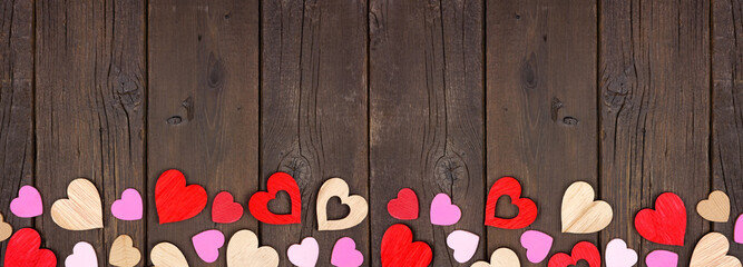 Wall Mural - Valentines Day bottom border of wooden hearts. Top view on a dark wood banner background. Copy space.