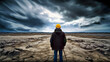 A person in a yellow cap and dark jacket stands in the middle of a vast, cracked landscape under a stormy sky