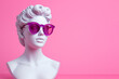 Ancient female greek sculpture wearing pink sunglasses. Greek goddess bust sculpture in glasses. Minimal composition, modern art, party, vacation and romantic concept. Copy space for text