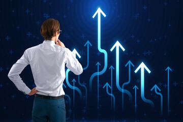 Canvas Print - Back view of young businessman looking at growing blue business chart arrows on blurry background. Success, trend and financial growth concept.