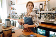 © maxbelchenko - Portrait of a smiling cafe owner using a digital tablet behind the bar counter in a modern coffee shop. A young barista takes an order using a tablet. Small business concept.