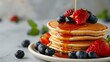 Pancakes with fresh strawberries, blueberry and maple syrup for a breakfast, honey pouring on delicious homemade pancakes with copy space.