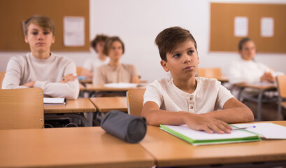 Portrait of upset tired teenage schoolboy sitting in classroom secondary school, learning lessons