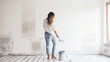 A young woman is happily renovating a newly purchased house. Paint the walls white.