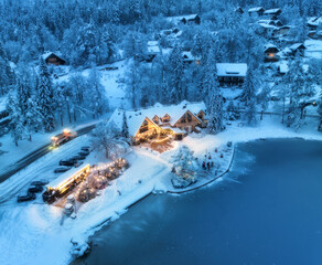 Sticker - Aerial view of illuminated houses in fairy village in snow, forest, Jasna lake, street lights at winter night. Top view of alpine countryside, snowy pine trees, road at dusk. Kranjska Gora, Slovenia