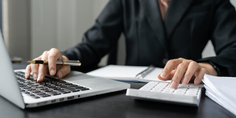 Wall Mural - Businesswoman using a calculator to calculate numbers on a company's financial documents, she is analyzing historical financial data to plan how to grow the company. Financial concept