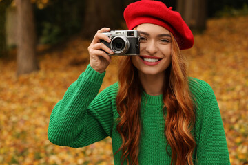 Poster - Smiling woman with camera taking photo in autumn park