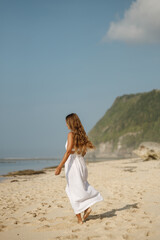 Wall Mural - Happy young woman wearing beautiful white dress is walking on the beach. Summer beach vacation concept, walk at the sandy beach