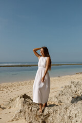 Wall Mural - Happy young woman wearing beautiful white dress is walking on the beach. Summer beach vacation concept, walk at the sandy beach