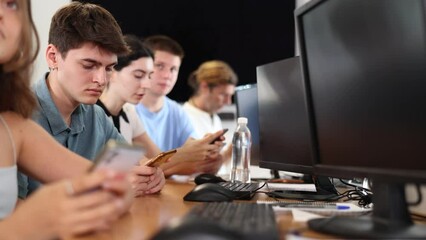 Wall Mural - Serious focused young student studying together with coursemates in computer workshop, actively using smartphone to access online learning materials. High quality 4k footage