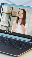 Wall Mural - Vertical video. Virtual meeting. Internet conference. Laptop with smiling business woman on screen talking at corporate online chat call at home office workspace.