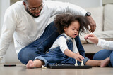 Fototapeta Nowy Jork - Cute little kid playing chess board toy as her parent sitting by. Multiracial family joyful game together with daughter child at home. Multiethnic girl enjoy playing chess pieces with her dad and mom.