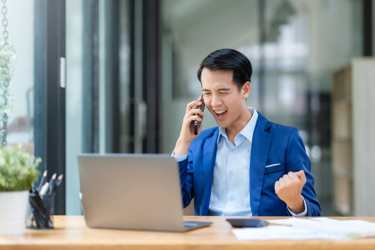 Successful Asian businessman receives good news from mobile phone. Happy asian businessman raising hands with victory smiling happily with smart phone. The concept of success at work.