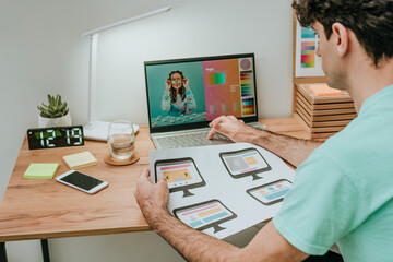 Web designer holding document and working on laptop in office