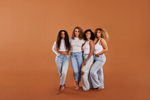 Diverse Women In White Tops And Jeans Standing On An Orange Backdrop