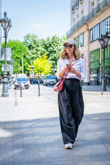 Poster - Full length of mid aged woman messaging on smartphone and walking on the street