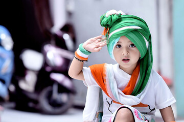 Wall Mural - Cute Asian Indian baby girl wearing white t-shirt, tricolor turban and band in hand looking at the camera directly in salute position celebrating 15th Aug  or 26th January 