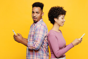 Wall Mural - Side view young sad shocked couple two friends family man woman wearing purple casual clothes together hold in hand use mobile cell phone stand back to back isolated on plain yellow orange background.