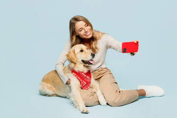 Wall Mural - Full body young owner woman with her best friend retriever dog wear casual clothes doing selfie shot on mobile cell phone isolated on plain light blue background studio. Take care about pet concept.