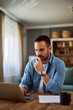 © Jelena - A focused young adult male writer revising his work on a laptop sitting at a desk with his hand to his chin.