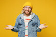 Young mistaken sad blond man wears denim shirt hoody beanie hat casual clothes spread hands shrugging shoulders looking puzzled isolated on plain yellow background studio portrait. Lifestyle concept.