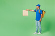Full body profile delivery guy employee man in blue cap t-shirt uniform workwear yellow thermal food backpack work as dealer courier hold paper bag isolated on plain green background Service concept