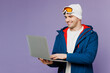Skier smiling IT man wears warm blue windbreaker jacket ski goggles mask hat hold use work on laptop pc computer spend extreme weekend winter season in mountains isolated on plain purple background.
