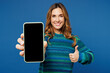 Young woman she wears knitted sweater casual clothes hold in hand use mobile cell phone with blank screen workspace area show thumb up isolated on plain blue cyan color background. Lifestyle concept.